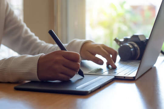 Young female graphic designer using digital tablet with electronic pen and work on laptop computer  at office. 
