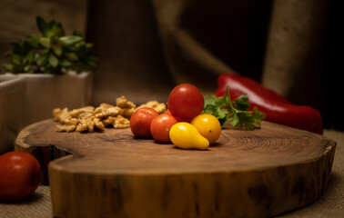 Close-up of cherry tomatoes on a wooden board with various vegetables and ingredients behind.