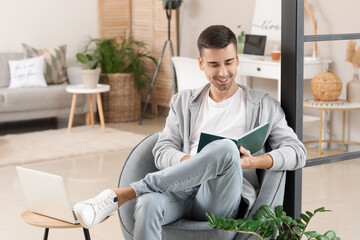 Young man with book sitting in armchair at home