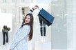 Cheerful girl with shopping bag walks through mall. Happy beautiful young woman with purchases. Black Friday discounts