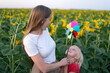 Young mom and son are walking in sunflower field with windmill toy. Green energy concept. Happy family