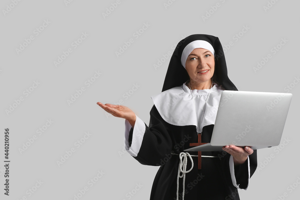 Mature nun with laptop on grey background