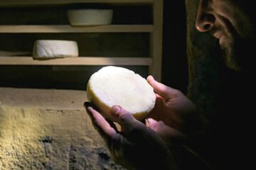 Cropped view of farmer looking at homemade cheese in dark cellar 