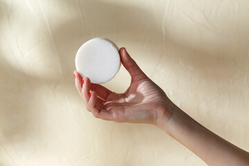 natural cosmetics, hygiene and beauty concept - hand holding bar of craft soap on beige background