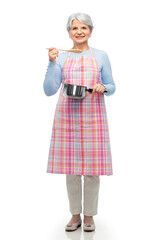 food cooking, culinary and old people concept - portrait of smiling senior woman in kitchen apron with pot and spoon over white background