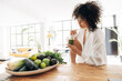 © Daniel - Young african american pretty woman relaxing in kitchen while having a green juice with bamboo straw in the morning. Detox. Cleanse.