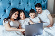 © Тарас Нагирняк - Happy family with kids lies on bed and watching something on laptop.Laughing and fun.