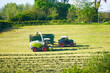 Two agricultural vehicles harvesting hay. Collecting hay for silage. Hilly green landscape.