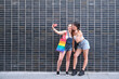 Two women taking a selfie sticking out their tongue, with a smartphone. LGBT people.