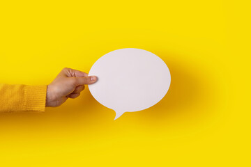 Hand holding a white round blank speech bubble over yellow background