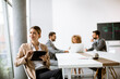 © BGStock72 - Young woman sitting by the table with digital tablet in modern office in front of her team