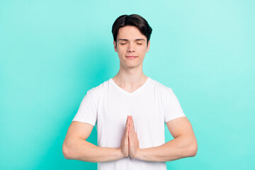 Sticker - Photo of relax brunet hairdo millennial guy hold hands closed eyes wear white t-shirt isolated on vibrant teal color background