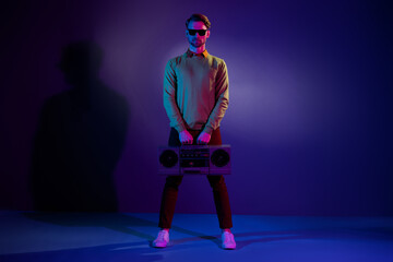 Poster - Full size photo of young trend guy stand with boom box wear eyewear sweater pants isolated on blue color background