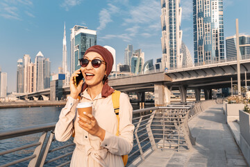 Asian Woman in a headscarf drinking coffee and talks and gossips on the phone with a friend on the Dubai Walk Canal