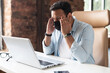 © Vadim Pastuh - Suffering from headache indian man in protective medical mask, tired and weary male employee sits in front of laptop and holds temples, feels viral disease symptoms
