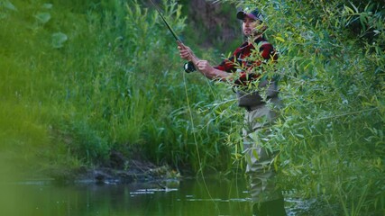 Wall Mural - Fly fishing. Angler fishing on the bushy coast and casts the line downstream the narrow creek