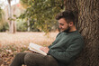 © Joaquin Acosta - Young Caucasian man sitting next to the tree and reading a book