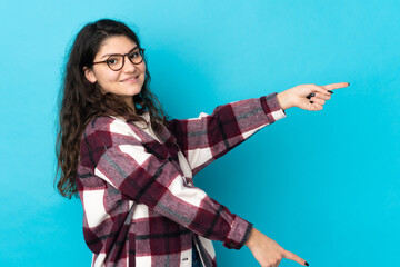 Teenager Russian girl isolated on blue background pointing finger to the side and presenting a product