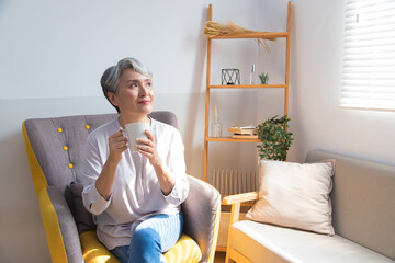 Wall Mural - Senior woman holding a cup of coffee or tea relaxing at home in the morning.