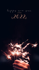 Poster - Make a wish new year 2022 with hand holding burning Sparkler firework blast with on a black bokeh background at night,holiday celebration event party.vertical ratio