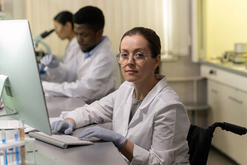 Sticker - Confident female chemist using computer by workplace against two colleagues