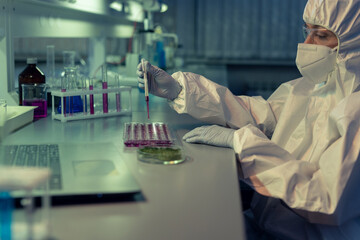 Sticker - Scientist in coveralls, gloves, eyeglasses and respirator dropping purple fluid into one of tiny containers