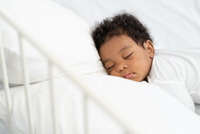 Black African American Baby Sleeping On A White Mattress.