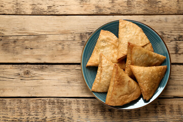 Fresh delicious crispy samosas on wooden table, top view. Space for text