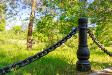 Black Old Post With Chains On A Background Of Green Grass And Wood