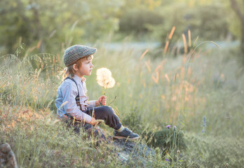 a boy sits in a field with a bouquet of white dandelions and smiles. the concept of childhood and happiness