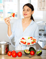 Portrait of woman tasting freshly made vegetable salad in kitchen