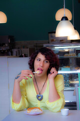 Wall Mural - Young transgender eating dessert in a cafe with a yellow shirt on, with makeup on portrait