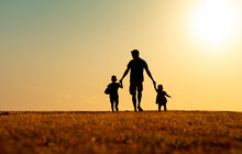 Silhouette Of Father And Children Holding Hands Walking Outdoors In The Park. Fatherhood, And Childhood Concept. 
