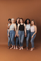 Wall Mural - Studio shot of six women standing together holding their hands and looking at camera over brown background