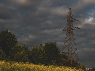 old Electric pole and electric cable on a field in the countryside with cloudy and blue sky.