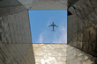 A selective focus shot of an airplane flying seen from the ground through the hole in the roof of a building
