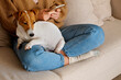 © Evrymmnt - Cropped shot of adorable jack russell terrier pup sitting with its female owner. Unrecognizable woman wearing knitted sweater and mom jeans with cute doggy on her lap. Close up, copy space, background