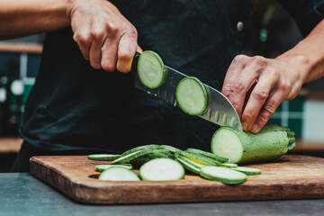 Wall Mural - Chef in a black uniform chopping zucchini on a wooden board