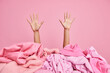 Female hands raised up from pile of unfolded pink clothes. Unrecognizable cluttered woman poses indoor. Monochrome shot. Revision of clothing at home. Disorder and mass. Wardrobe decluttering