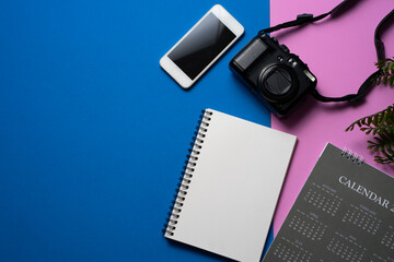 concept of travel vacation trip and long summer weekend planning with camera , calendar and mobile phone on blue and pink table background