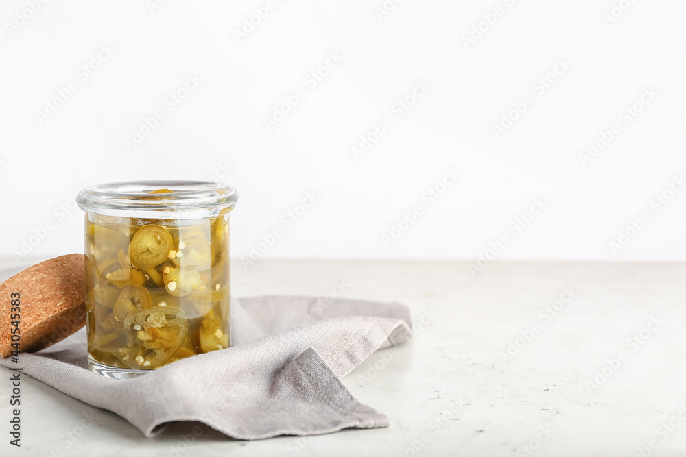 Glass jar with canned jalapeno on light background