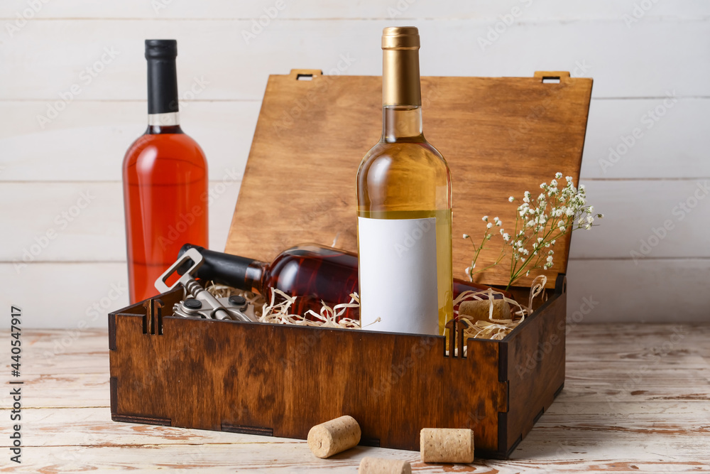 Box with bottles of wine and corkscrew on light wooden background