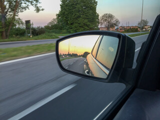 Poster - Rear view mirror showing the road at sunset - trees and the sky on the roadside