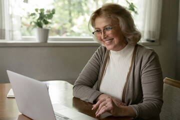 Wall Mural - Happy senior Caucasian woman look at laptop screen talk speak on video call on device from home. Smiling old female use computer have webcam digital virtual event. Communication, technology concept.