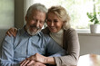 © fizkes - Smiling old middle-aged Caucasian man and woman sit hugging cuddling enjoy happy maturity life together at home. Excited optimistic mature couple spouses show love and care in family relationships.