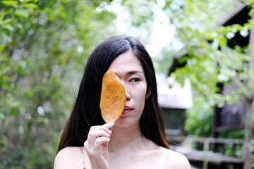 Asian woman is holding a yellow dry leaves in natural garden and summertime in Thailand