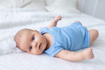 cute baby boy three months old in a blue bodysuit on a white bed at home