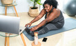 © Alessandro Biascioli - Young African curvy woman doing pilates online fitness class with laptop at home - Sport wellness people lifestyle concept