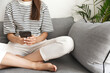 © Liubov Levytska - Cropped shot of woman sitting on sofa comfortable, using smartphone, holding mobile phone, sit with legs crossed at home