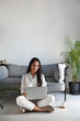 Vertical portrait of freelancer at home, asian girl student working with computer, drinking coffee tea and typing. Young woman studying in living room, writing in blod and smiling